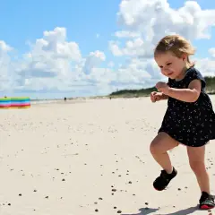 Radosne wakacje z dziećmi w Polsce. Mała dziewczynka biega po piaszczystej plaży, ciesząc się słońcem i chmurami na niebie.