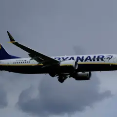 Samolot Ryanair z logo na ogonie leci na tle pochmurnego nieba. Może to być przypomnienie o konieczności sprawdzenia danych przed podróżą, bo ryanair zmiana nazwiska bywa kosztowna.
