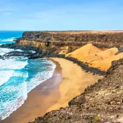 Plaża na Fuerteventurze, gdzie fale oceanu rozbijają się o skaliste wybrzeże. Czy na Fuerteventurę potrzebny jest paszport? Tak, jeśli podróżujesz spoza strefy Schengen.