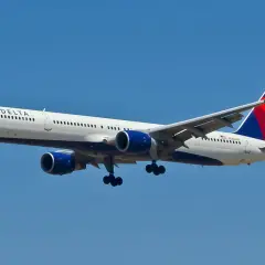 Boeing 757-300 linii Delta z wysuniętym podwoziem zbliża się do lądowania na tle błękitnego nieba.