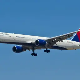Boeing 757-300 linii Delta z wysuniętym podwoziem zbliża się do lądowania na tle błękitnego nieba.