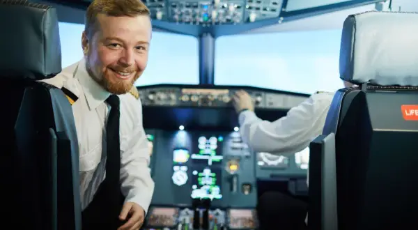 Uśmiechnięty pilot liniowy w kabinie samolotu, obok drugiego pilota obsługującego przyrządy.