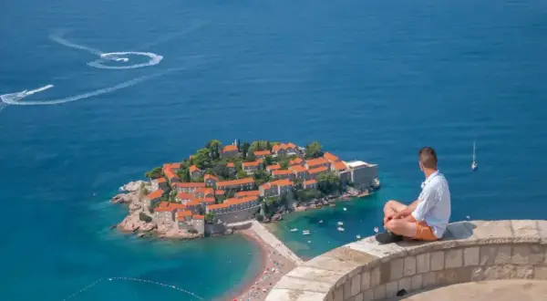 Mężczyzna siedzi na murze, podziwiając wyspę Sveti Stefan. Czy Czarnogóra jest bezpieczna? Tak, to spokojne miejsce na wakacje.