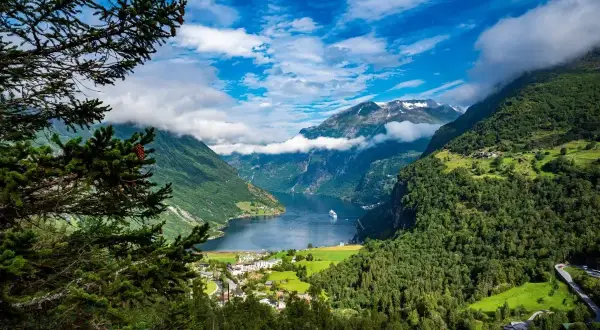Majestatyczne fiordy Norwegii z zielonymi zboczami, białymi chmurami i statkiem wycieczkowym na wodzie.