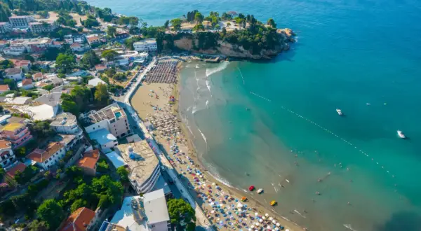 Majowa pogoda w Czarnogórze zachęca do plażowania. Widok z lotu ptaka na wybrzeże z turkusową wodą, piaszczystą plażą pełną leżaków i turystów.