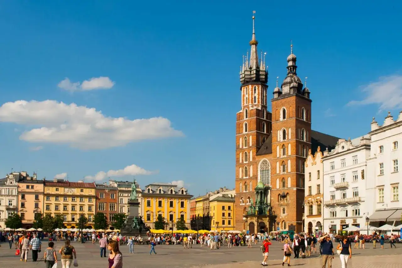 Rynek Główny w Krakowie, z Kościołem Mariackim i Sukiennicami. Mnóstwo ludzi spaceruje, a niebo jest błękitne. Ciekawe ciekawostki o Krakowie czekają na odkrycie!