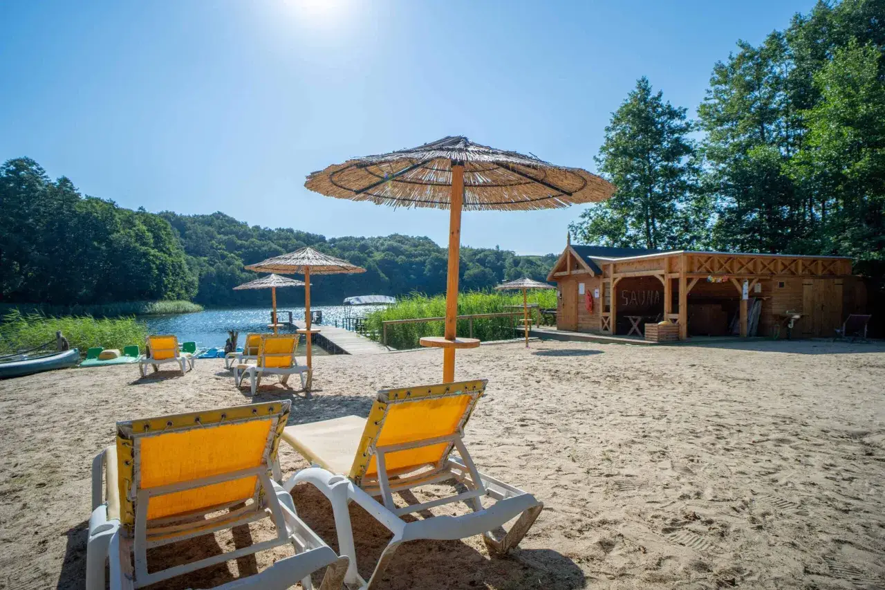 Idealne miejsce, gdzie z dzieckiem na weekend: piaszczysta plaża, jezioro, drewniana sauna i leżaki pod słomianymi parasolami.