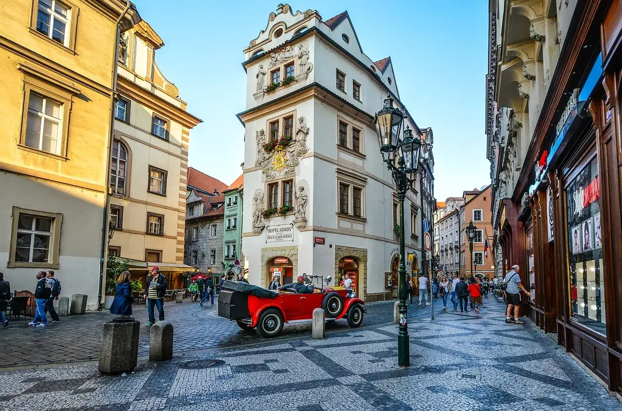Uliczka w Pradze z zabytkowym czerwonym kabrioletem. W tle kamienice, w tym Hotel Aurus z napisem