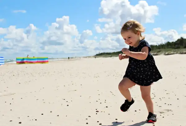Radosne wakacje z dziećmi w Polsce. Mała dziewczynka biega po piaszczystej plaży, ciesząc się słońcem i chmurami na niebie.