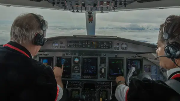 Dwóch pilotów w kokpicie, jeden wskazuje na ekran. Zastanawiasz się, ile zarabia pilot? To praca pełna odpowiedzialności.