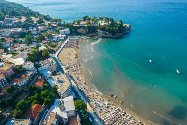 Majowa pogoda w Czarnogórze zachęca do plażowania. Widok z lotu ptaka na wybrzeże z turkusową wodą, piaszczystą plażą pełną leżaków i turystów.
