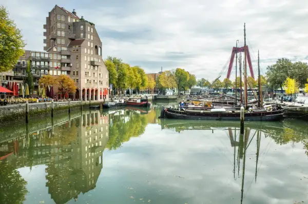 Widok na kanał z łodziami i nowoczesną architekturą, gdzie leży Rotterdam. W oddali czerwony most.