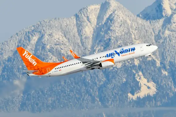 Boeing 737-900 linii Air North z charakterystycznym ogonem w barwach Yukon wzbija się na tle ośnieżonych gór.