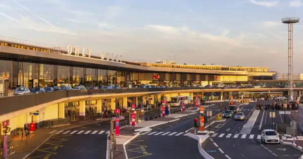 Lotnisko Orly-Ouest w Paryżu z samochodami i autobusem przed budynkiem.